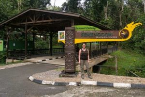 Farina steht unter dem Eingangsschild des Semenggho Wildlife Centre vor einem großen Unterstand an einem Weg im Park.