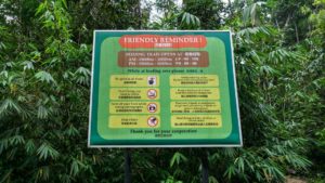 EIn grünes Schild mit Parkregeln vor einer grünen Blätterwand im Regenwald des Semenggoh Wildlife Centre.